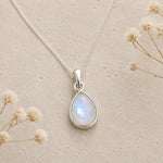 flatlay of a sterling silver moonstone necklace featuring a natural moonstone cabochon, bezel-set and pear-shaped pendant on a fine curb chain