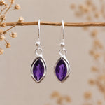 Silver earrings with marquise shaped purple amethyst gemstones on a branch with dried flowers.