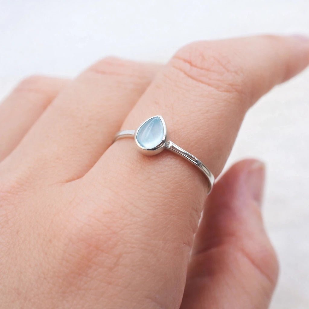 Silver ring with a blue natural topaz gemstone on a person's finger against a white background