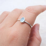Silver ring with a blue natural topaz gemstone on a person's finger against a white background