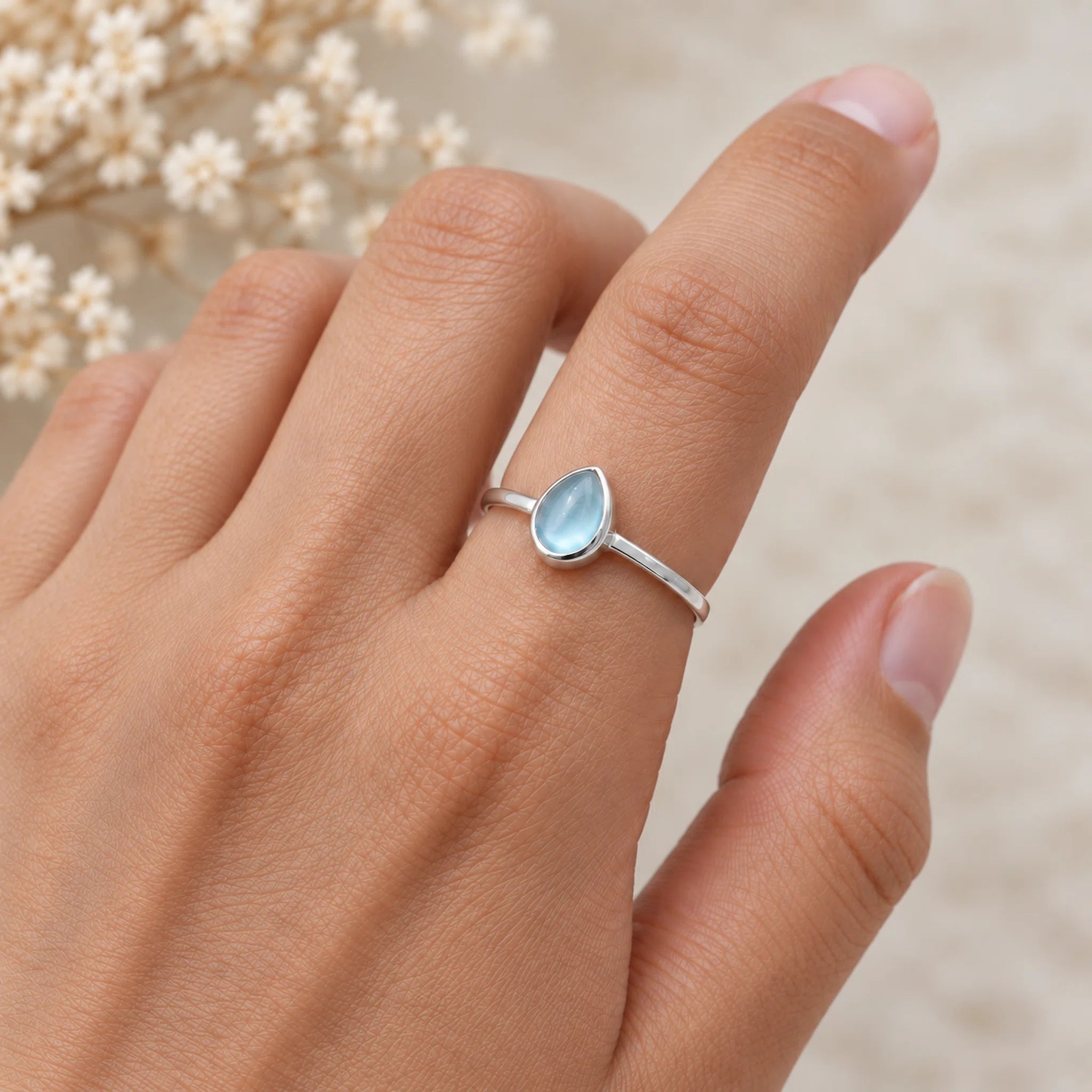 Silver ring November birthstone with a blue natural topaz gemstone on a person's finger against a white background