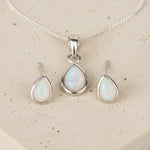 Sterling silver Opal pendant set with necklace and earrings on a beige stone surface