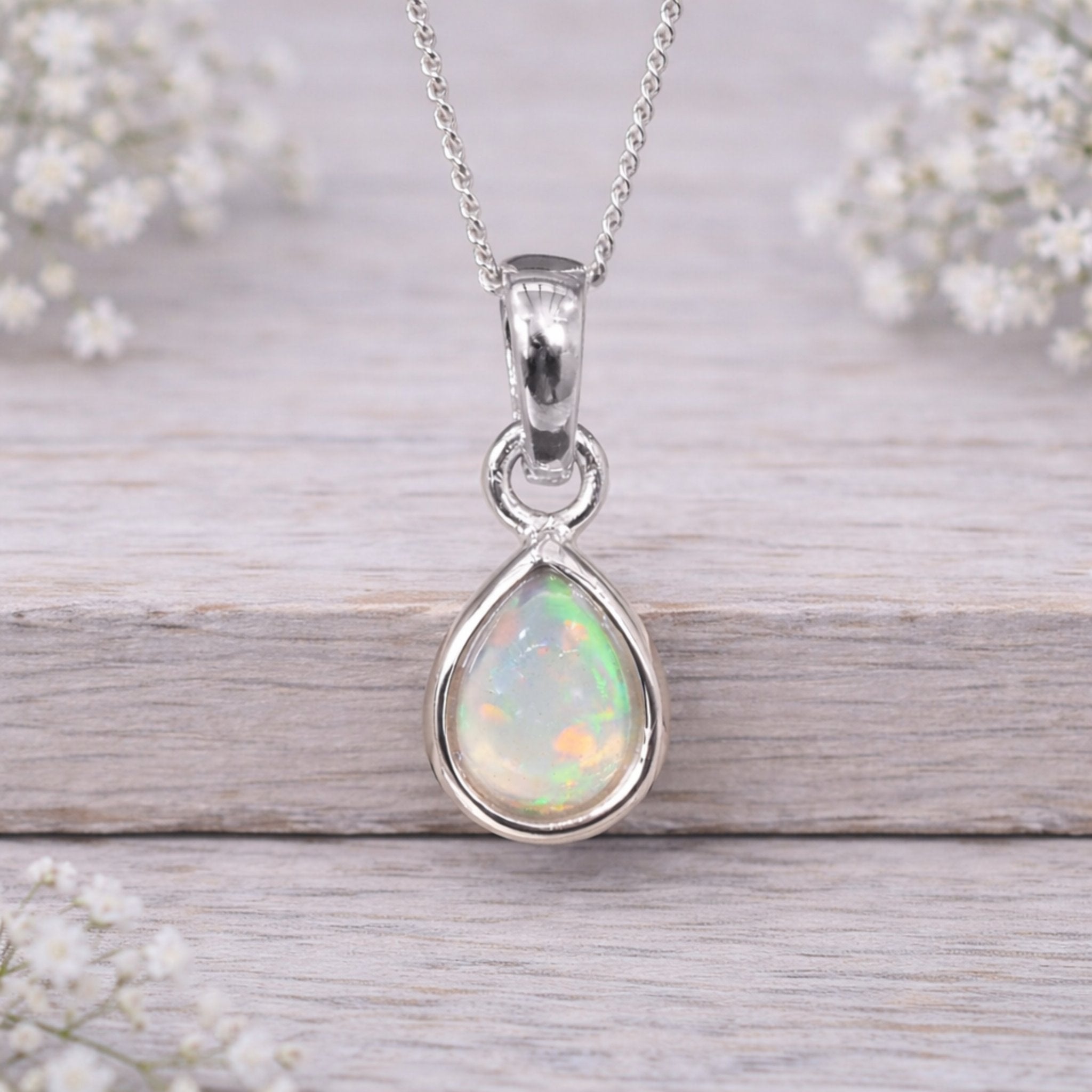 Opal pendant necklace on a wooden surface with flowers