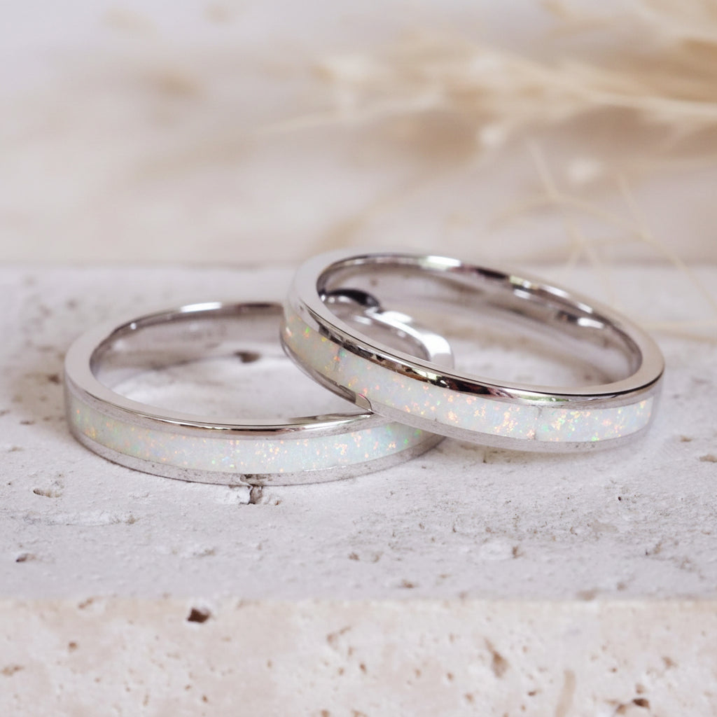 Two silver rings with opal inlay on a light stone surface