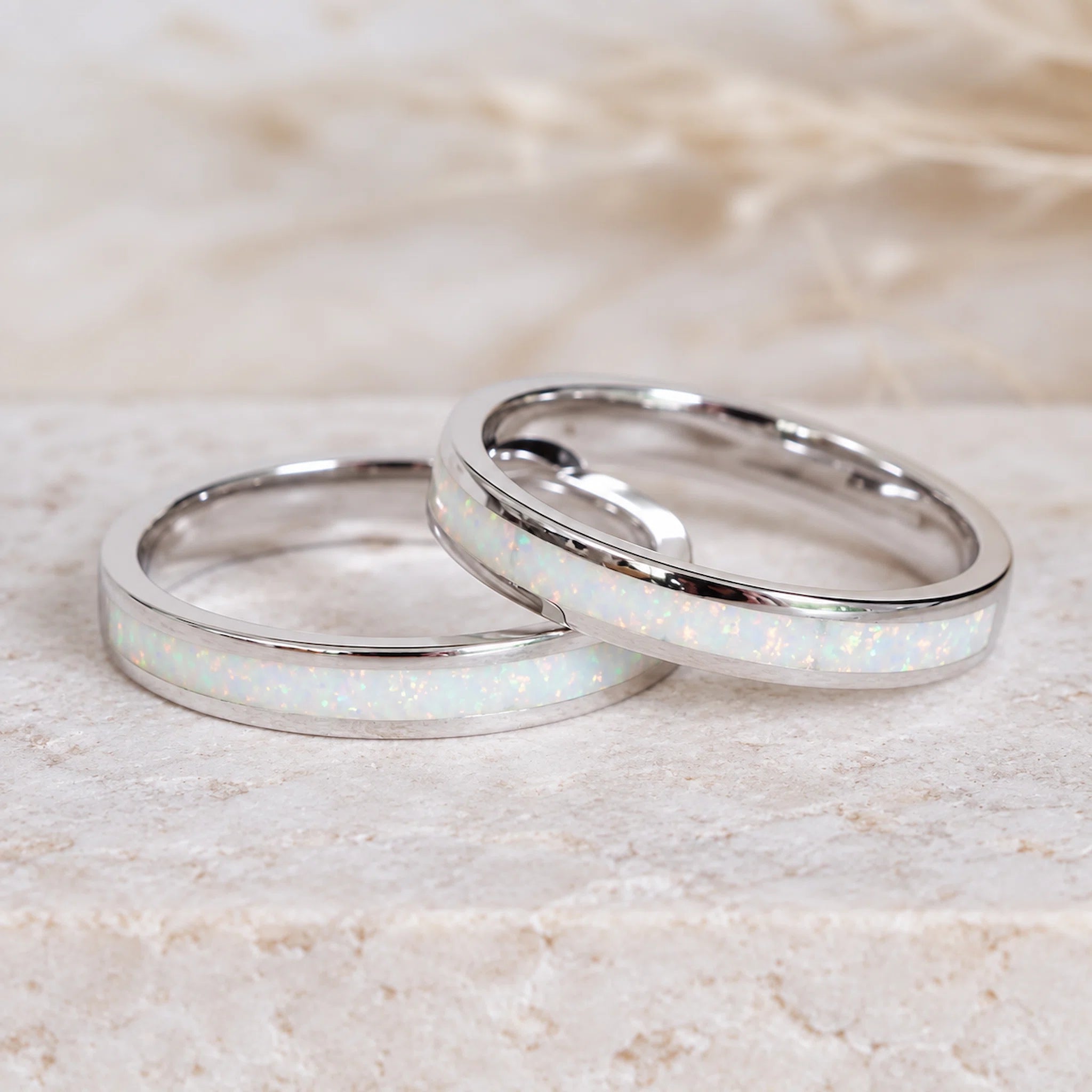 Two silver rings with opal inlay on a light stone surface