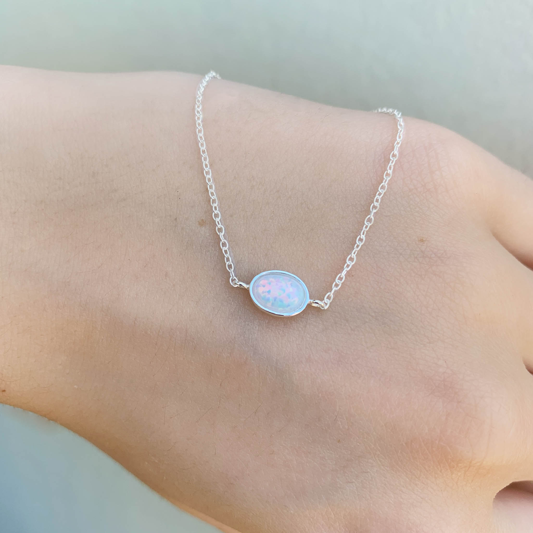 sterling Silver bracelet with an opal on a person's hand against a neutral background