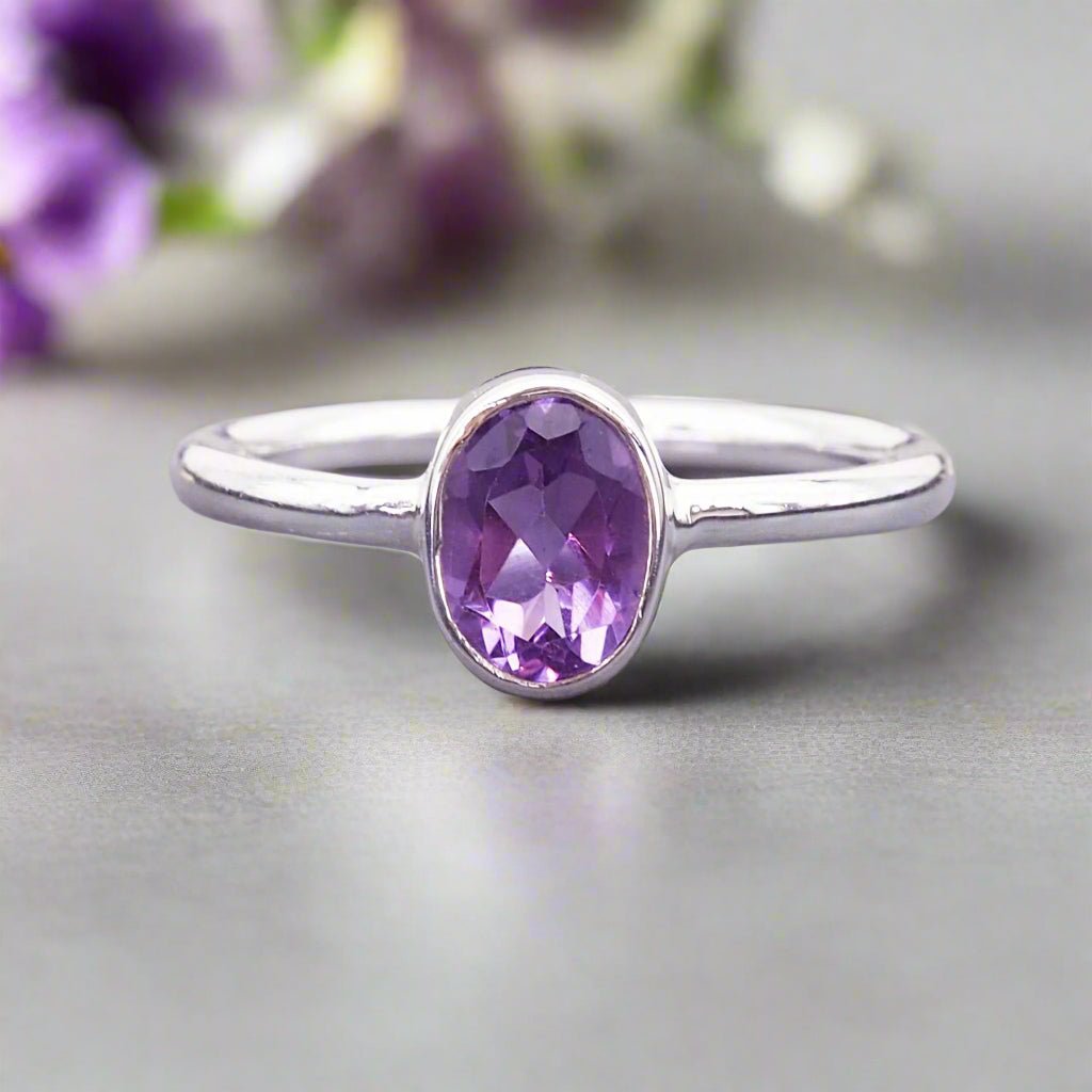 Sterling Silver ring with a natural amethyst gemstone on a grey surface with blurred purple flowers in the background