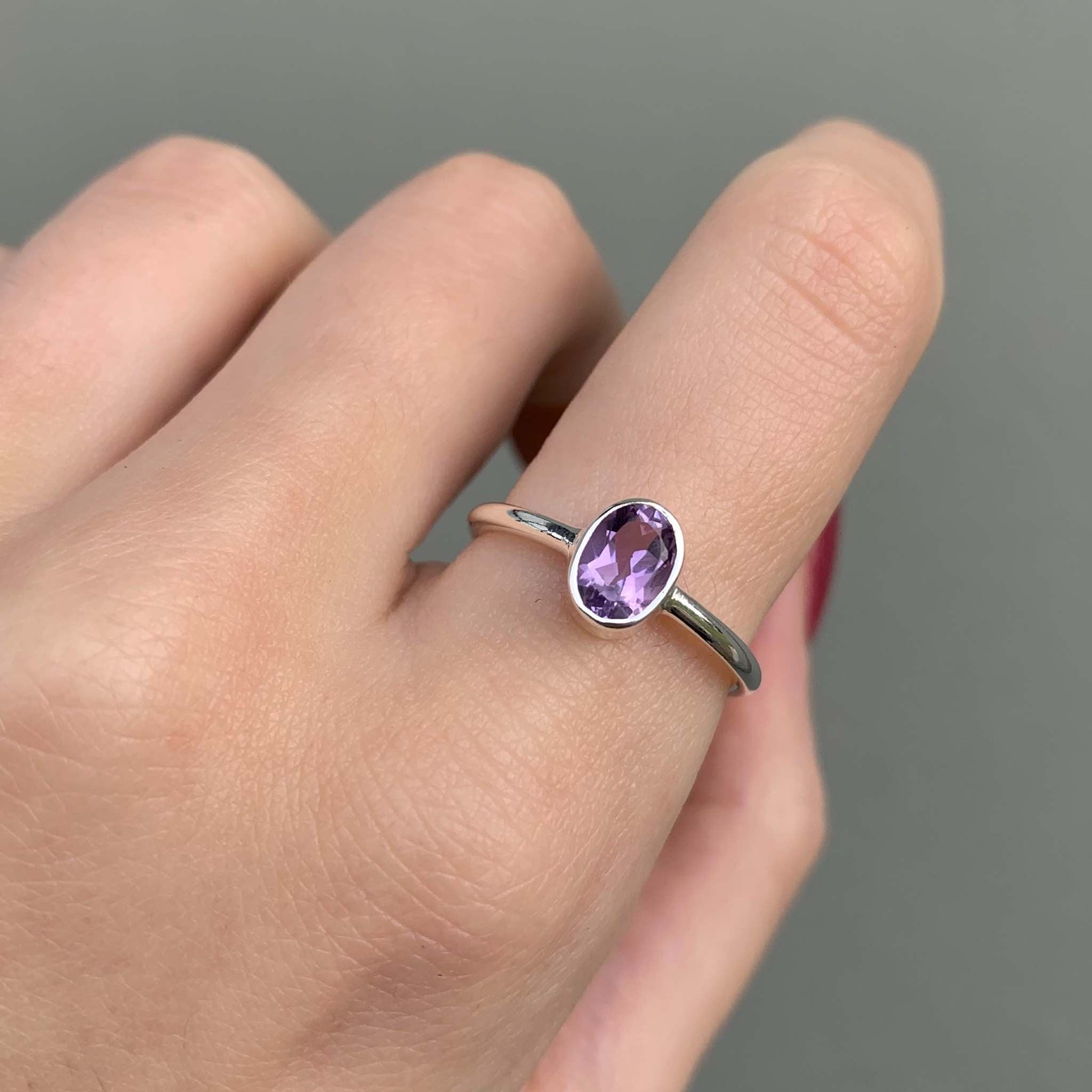 Sterling Silver ring with a purple amethyst gemstone on a finger against a grey background