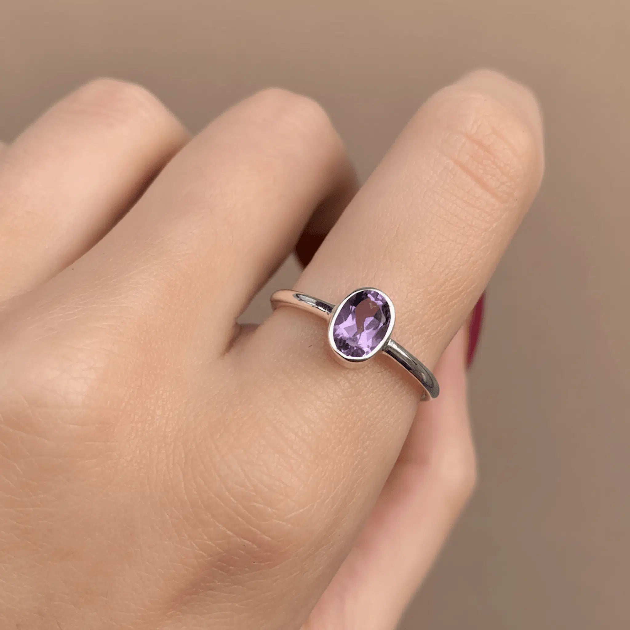 Silver ring with a purple amethyst gemstone on a finger against a beige background