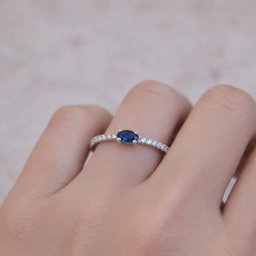 sterling silver Ring with a blue sapphire gemstone on a finger against a neutral background