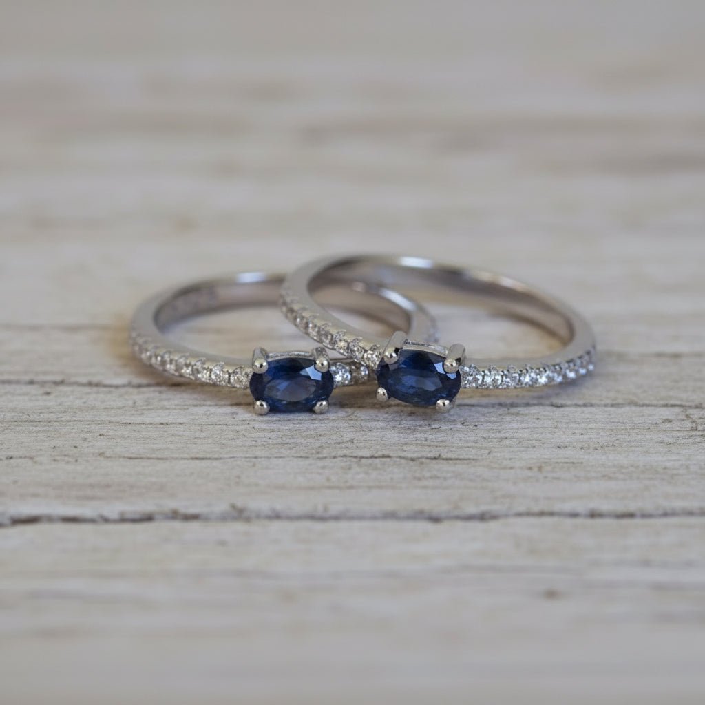 Two sterling silver rings with blue sapphire gemstones on a textured wood surface