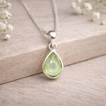 Green teardrop pendant on a silver chain with a wooden background