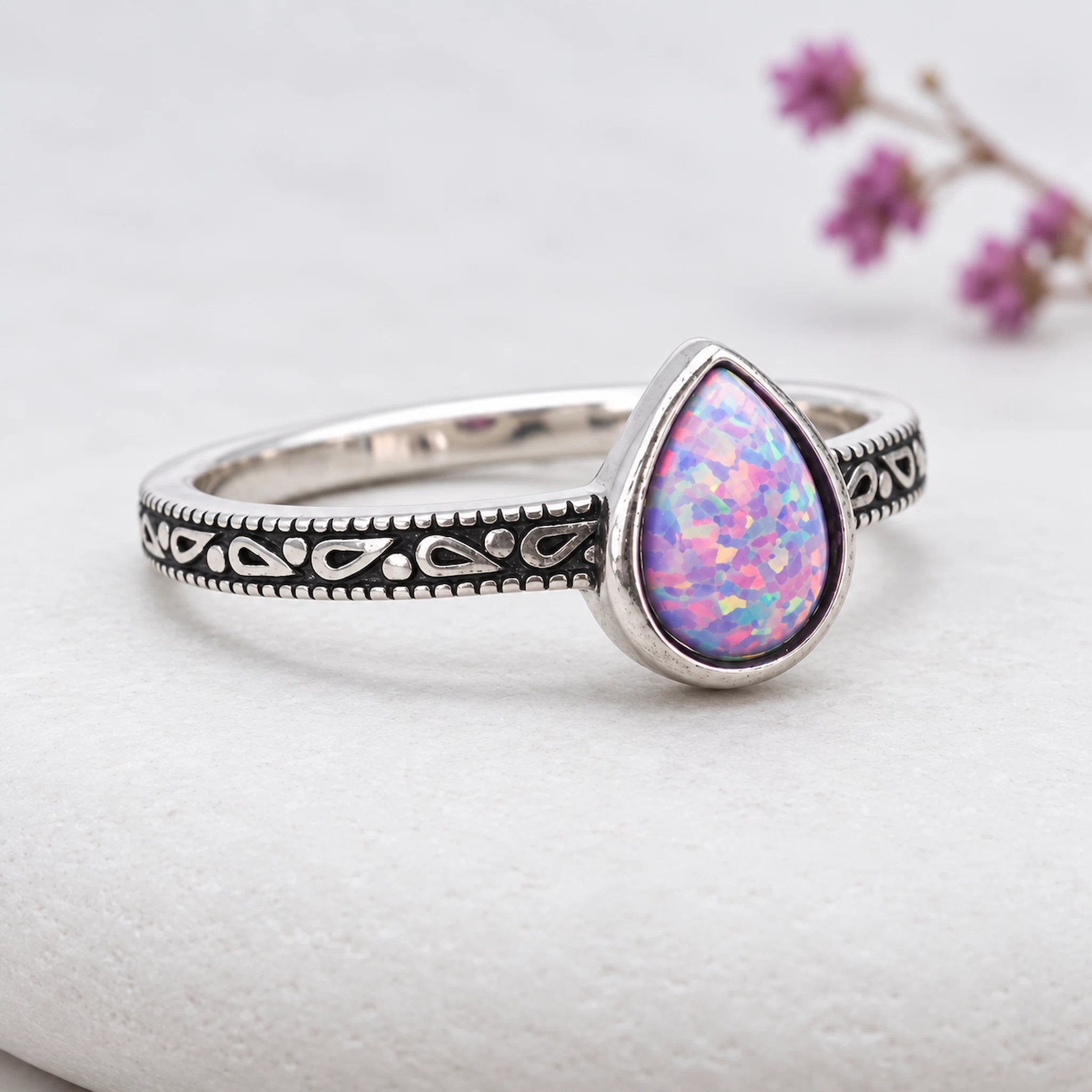 sterling Silver ring with a teardrop-shaped purple opal stone on a white surface with a purple floral background