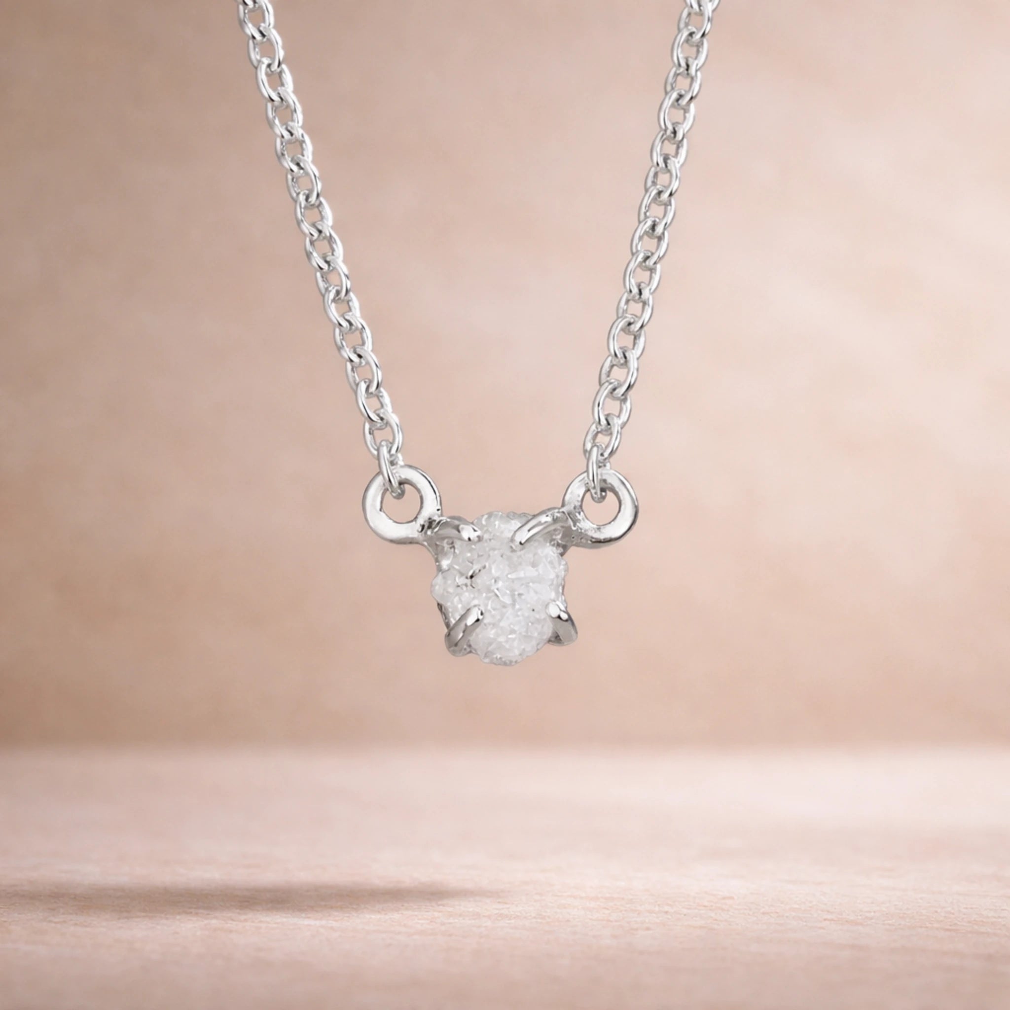 Sterling silver raw white diamond necklace hanging with a light warm background