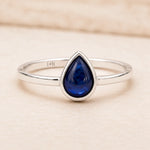 sterling Silver September birthstone sapphire ring with a blue teardrop-shaped natural sapphire gemstone on a light pink background