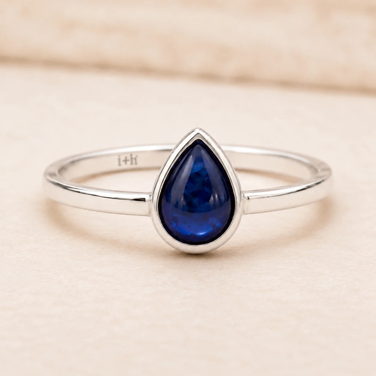 sterling Silver September birthstone sapphire ring with a blue teardrop-shaped natural sapphire gemstone on a light pink background