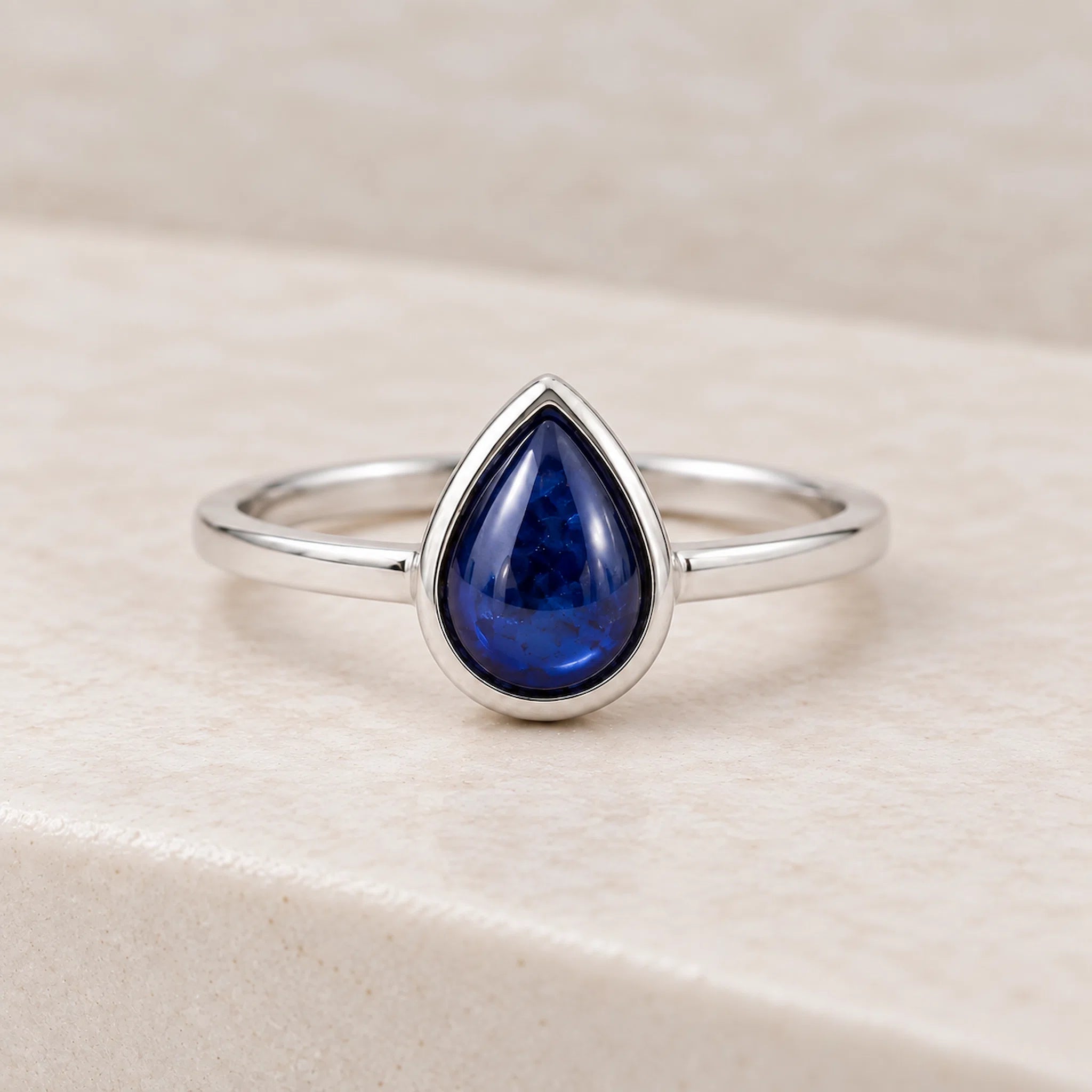 sterling Silver September birthstone sapphire ring with a blue teardrop-shaped natural sapphire gemstone on a light pink background
