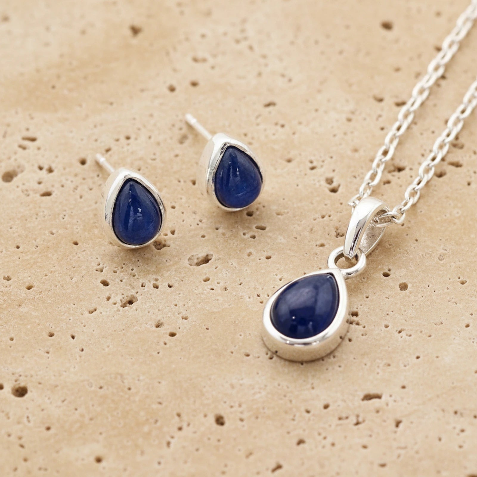 Jewellery set with september birthstone blue teardrop sapphire stones on a beige textured background