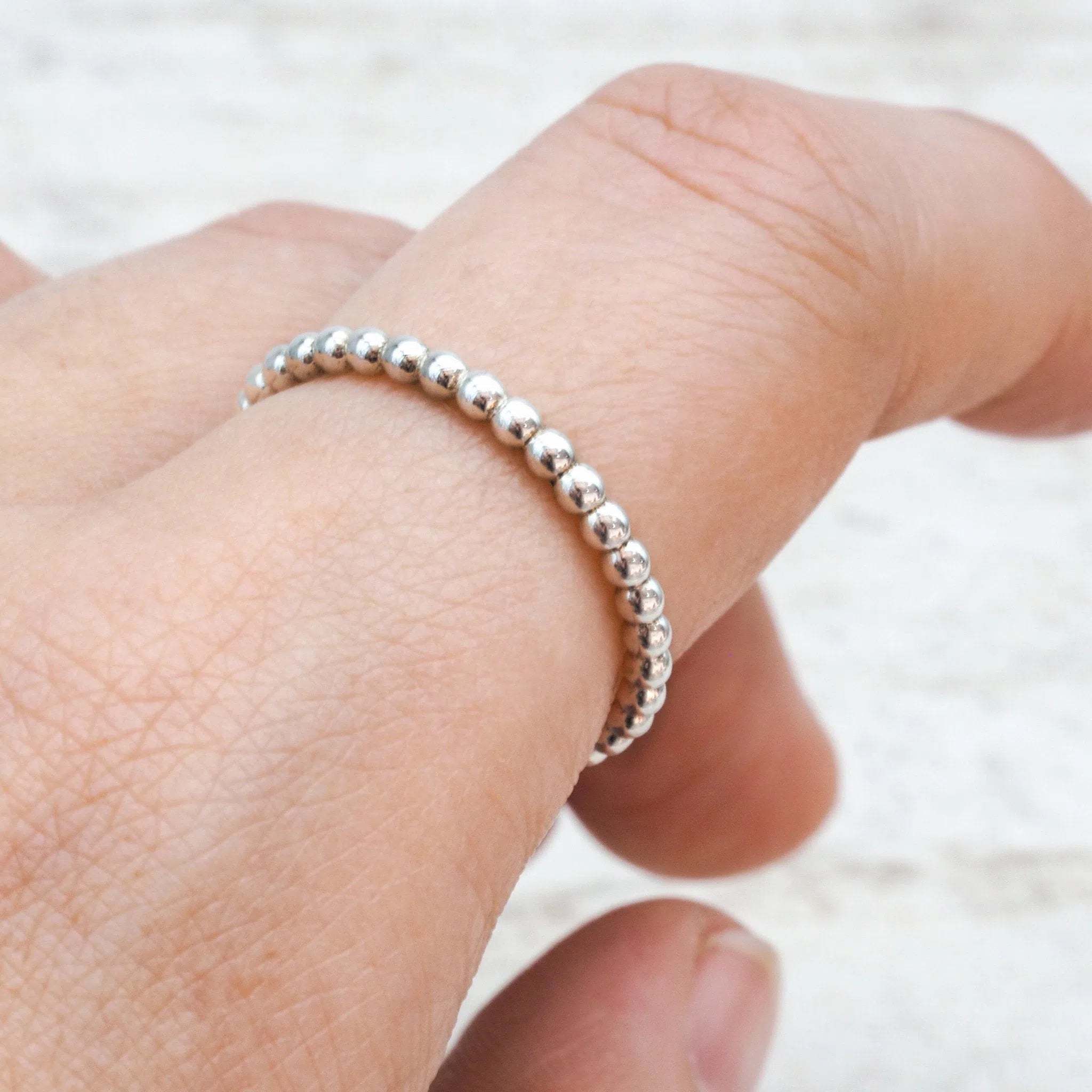 Sterling Silver beaded stacker ring on a finger with a blurred background