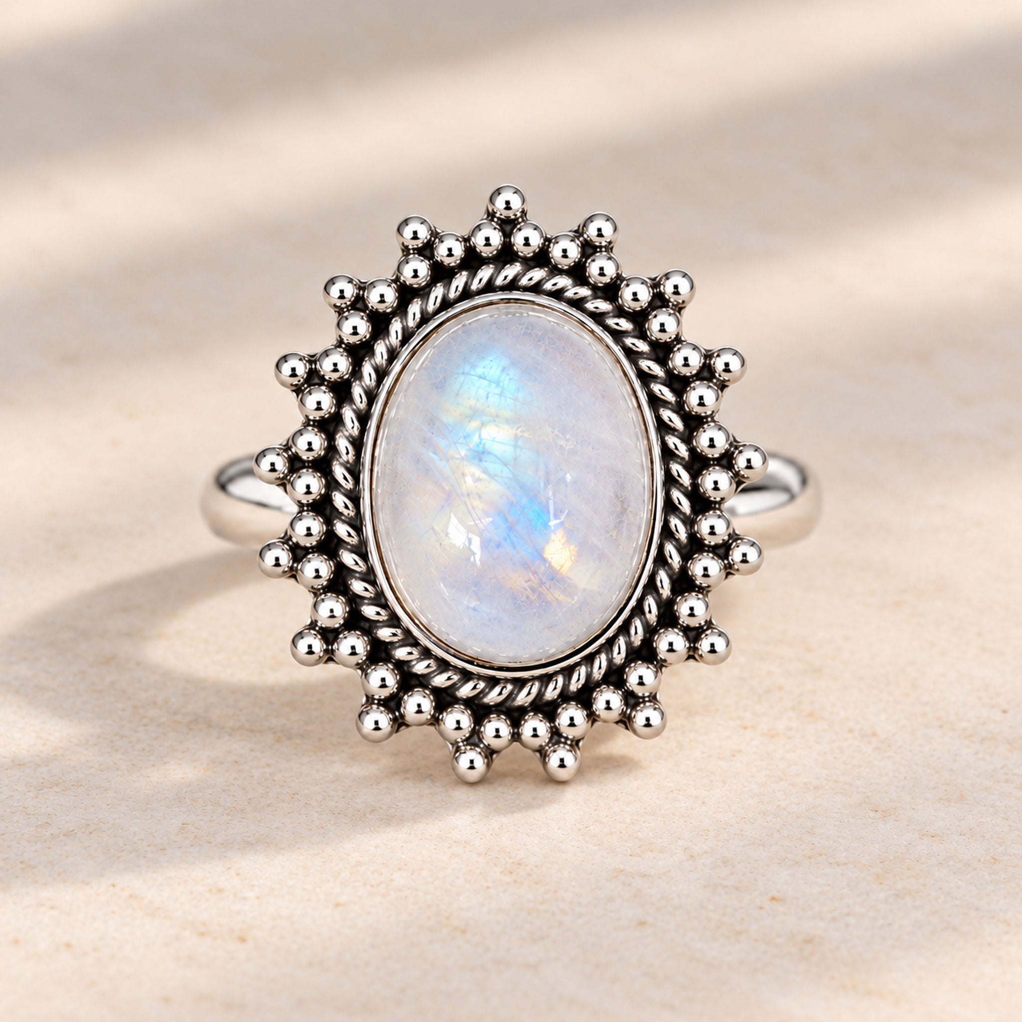 Sterling silver rainbow moonstone sun ring, front view on a warm stone surface