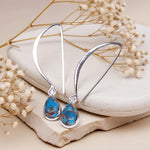 Silver earrings with blue turquoise stones on a stone surface with dried flowers.