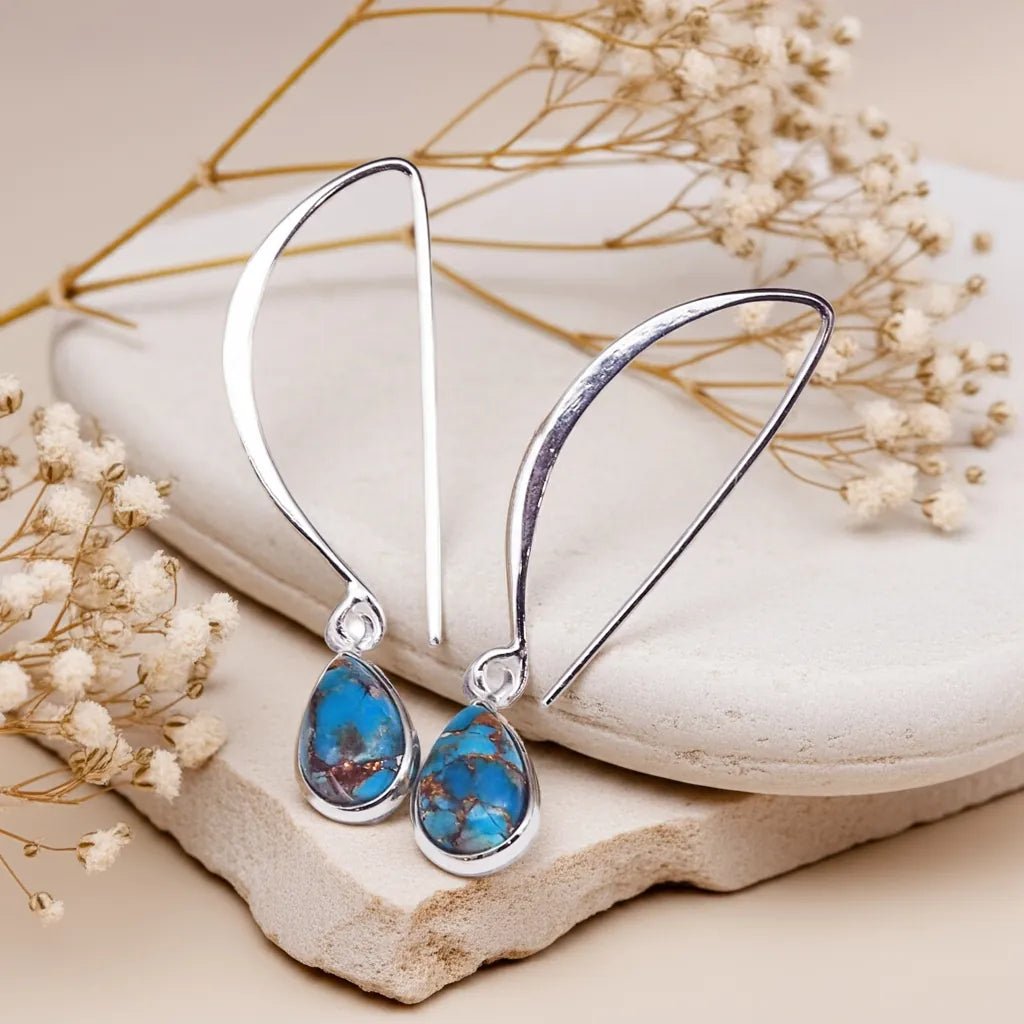 Sterling Silver turquoise earrings with blue turquoise gemstones on a stone surface with dried flowers.