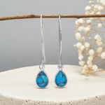 Teardrop-shaped turquoise earrings on a branch with a neutral background