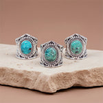Three turquoise stone rings with silver bands on a beige stone surface.
