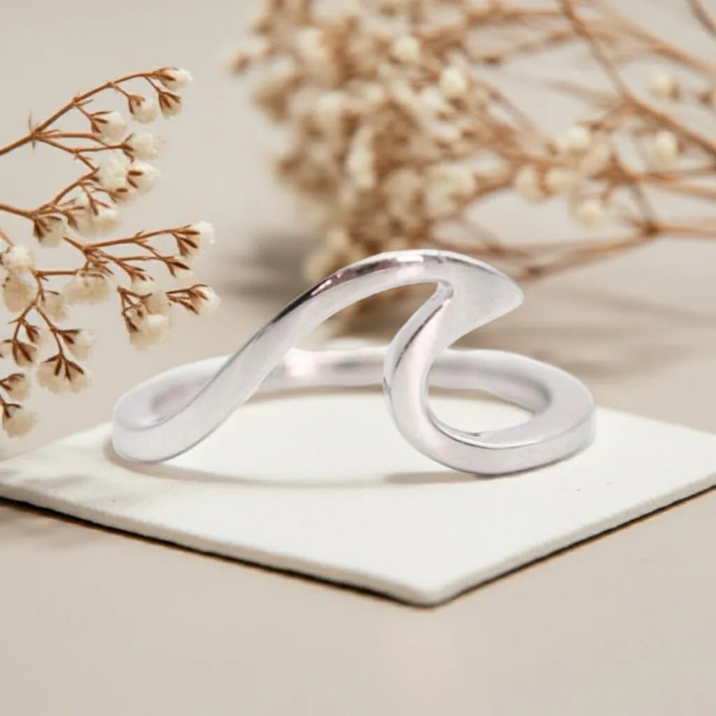 Silver ring with a wavy design on a white surface with beige flowers in the background