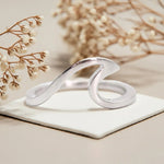 Silver ring with a wavy design on a white surface with beige flowers in the background