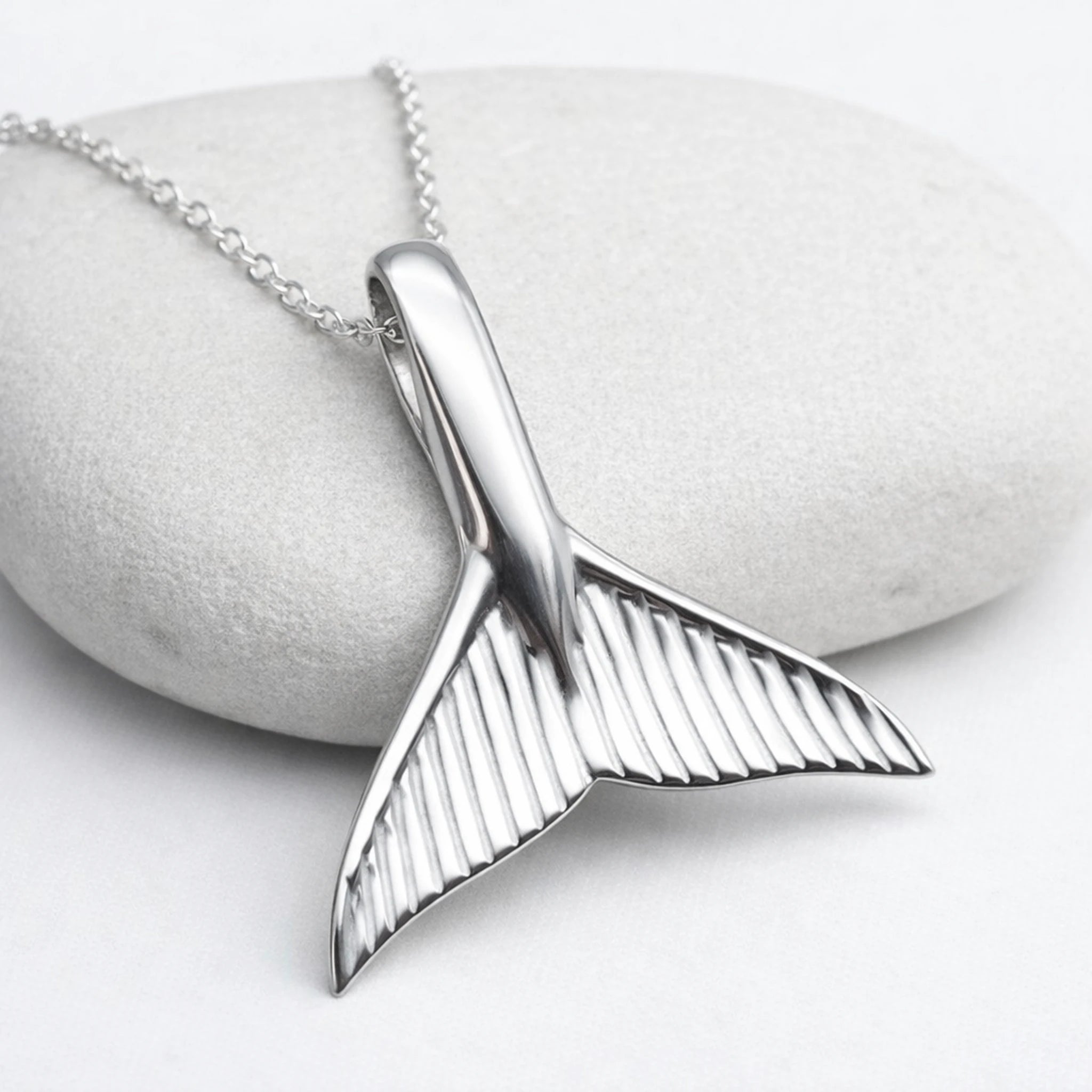Silver whale tail pendant on a chain against a stone background