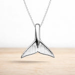 Sterling Silver whale tail pendant on a chain against a light background