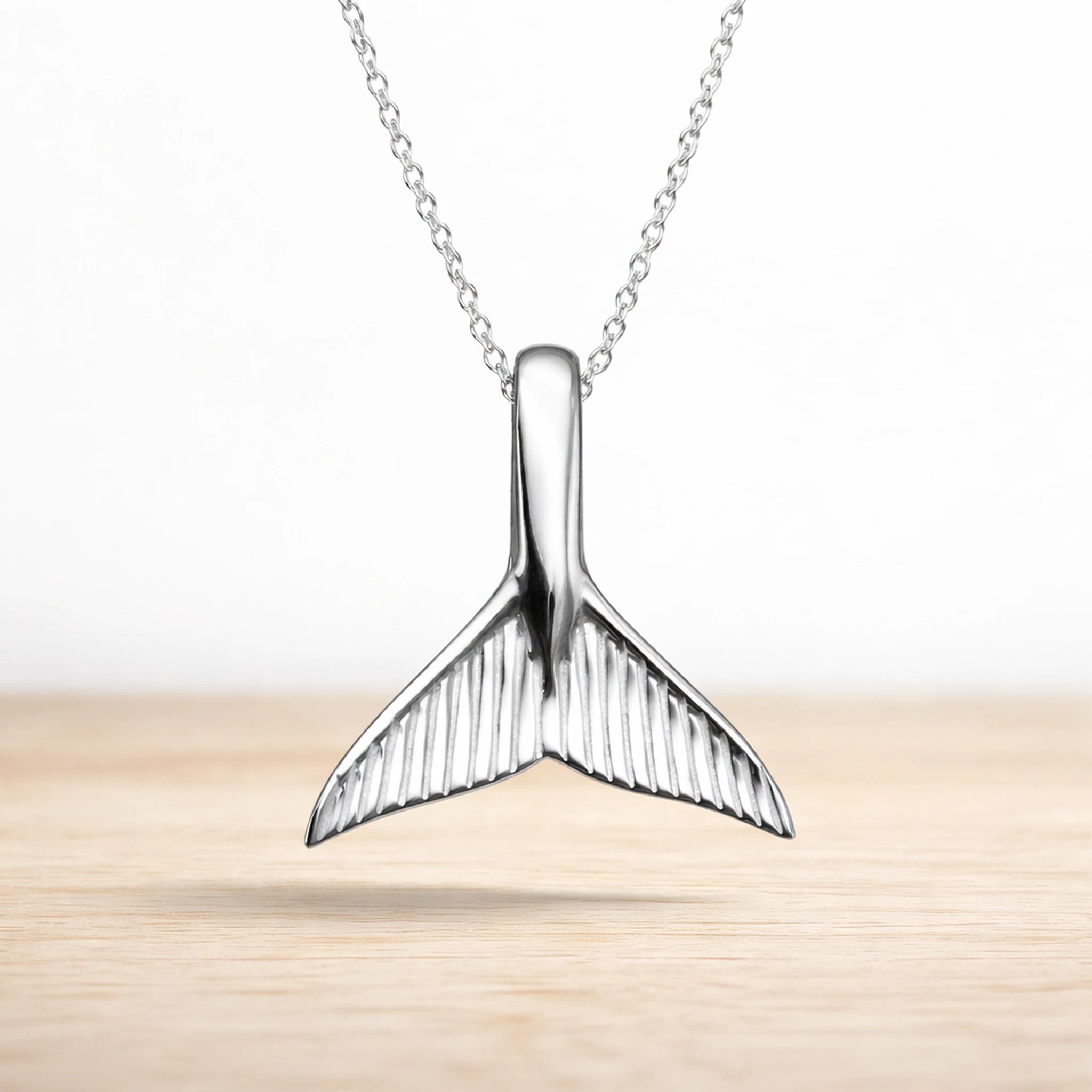 Sterling Silver whale tail pendant on a chain against a light background