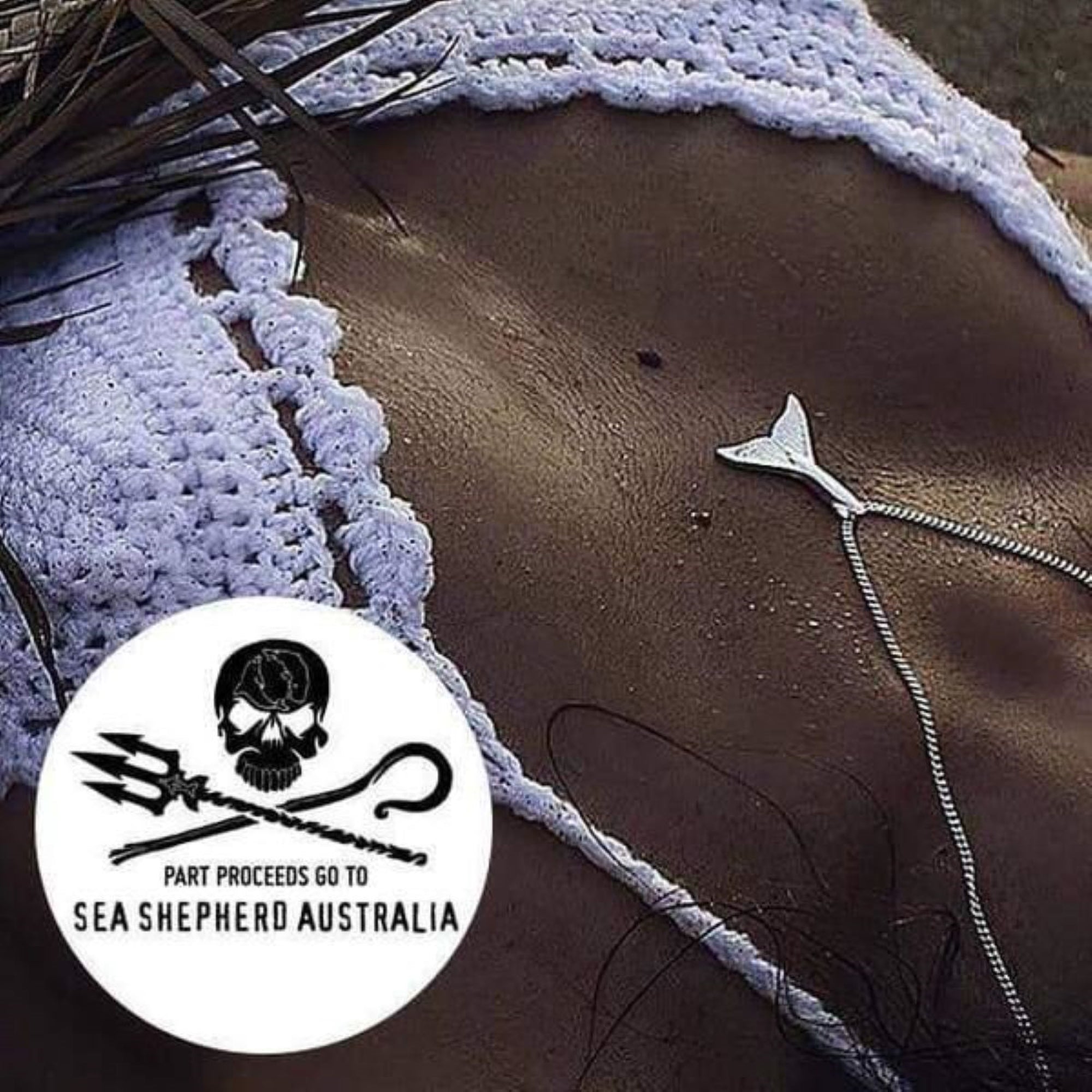 Close-up of a textured surface with a whale tail necklace and Sea Shepherd Australia logo