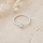 Silver ring with a central opal stone on a beige surface