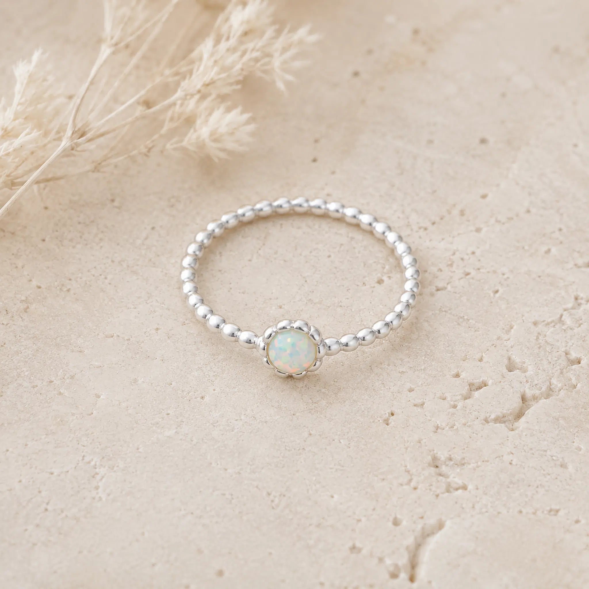 Silver ring with a central opal stone on a beige surface