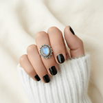 Hand with black nail polish wearing a silver moonstone decorative ring on a neutral background