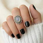 Hand with black nail polish wearing a decorative silver moonstone ring on a white background