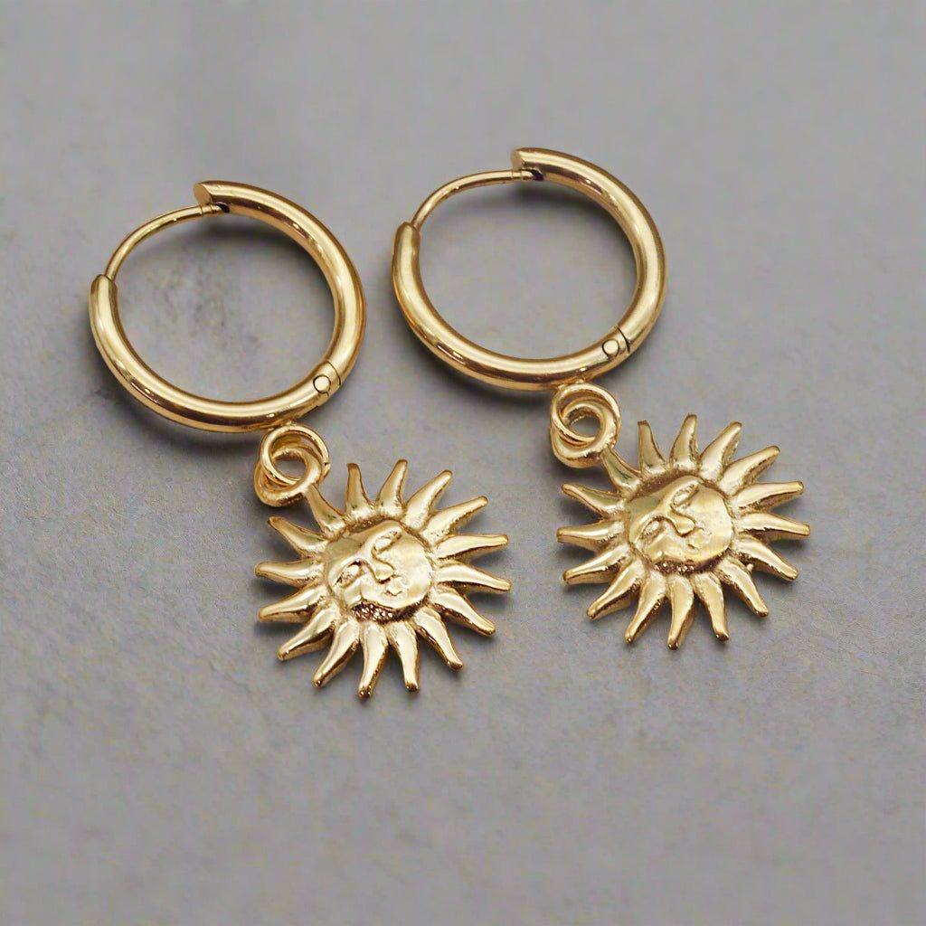 waterproof stainless steel, Sunburst Charm Gold Huggie Earrings laying on a grey surface