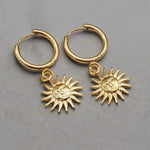waterproof stainless steel, Sunburst Charm Gold Huggie Earrings laying on a grey surface