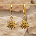 Sunburst charm gold huggie earrings in waterproof stainless steel hanging from a wooden rod