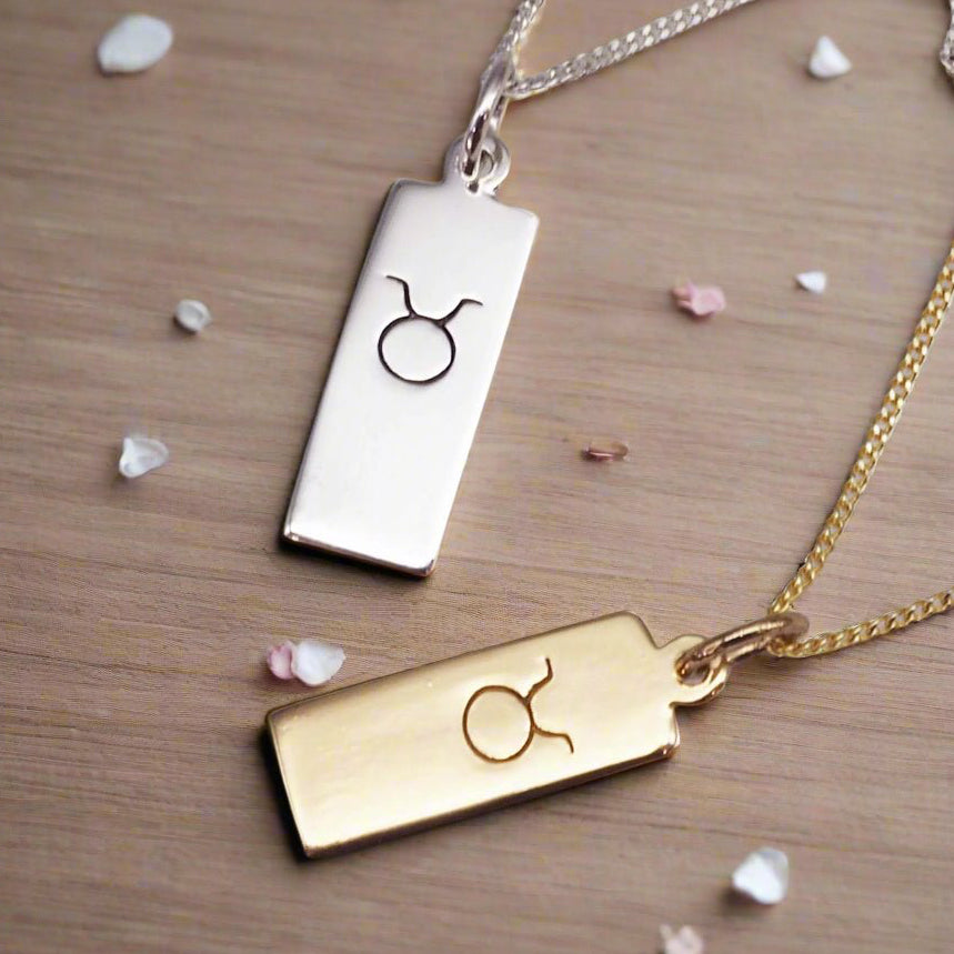 taurus zodiac necklaces in silver and gold on a wooden surface with petals
