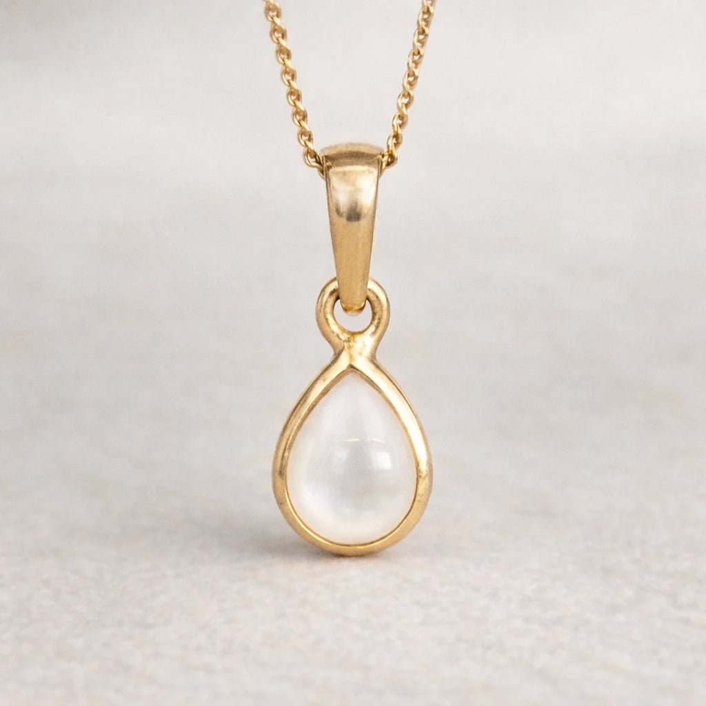 Gold pendant with a pearl gemstone on a light gray background
