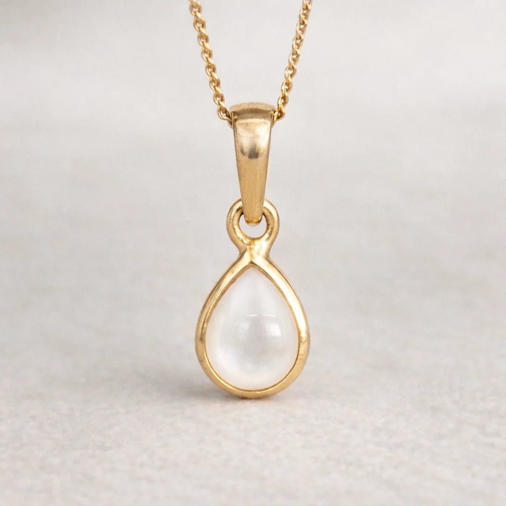 Gold pendant with a pearl gemstone on a light gray background