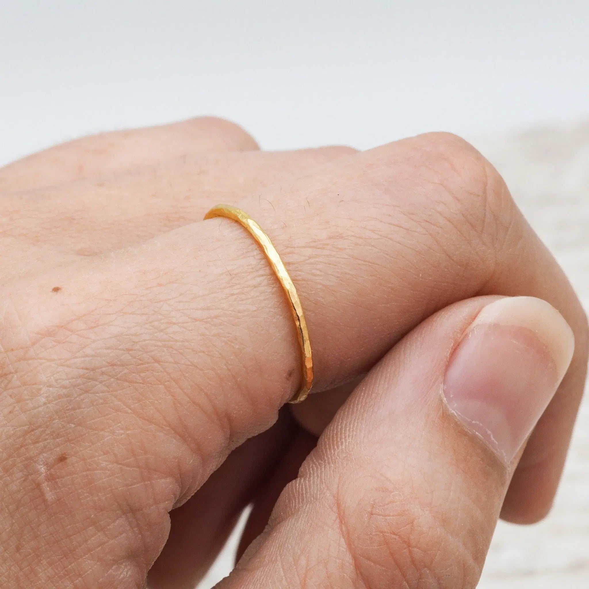 A thin, polished gold band ring worn on a person's finger, shown in a close-up shot.