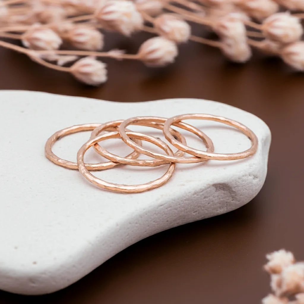 Rose gold rings on a white stone with dried flowers in the background