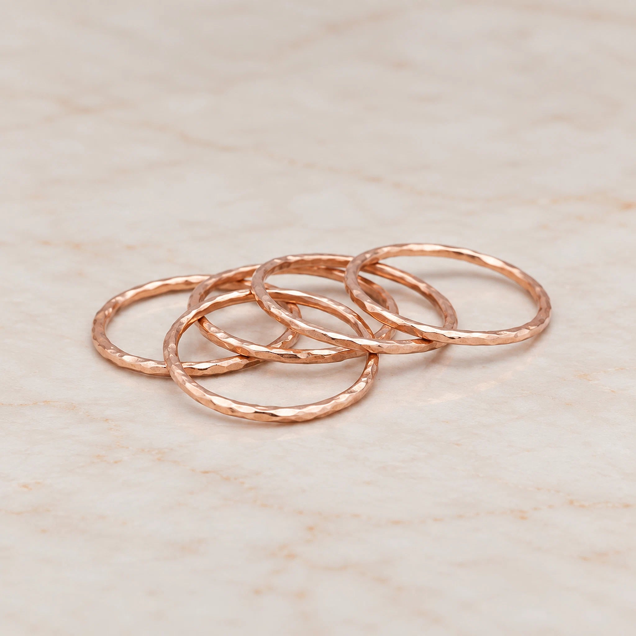 Rose gold hammered stacker rings arranged on a textured white surface, showcasing their delicate, shiny design.