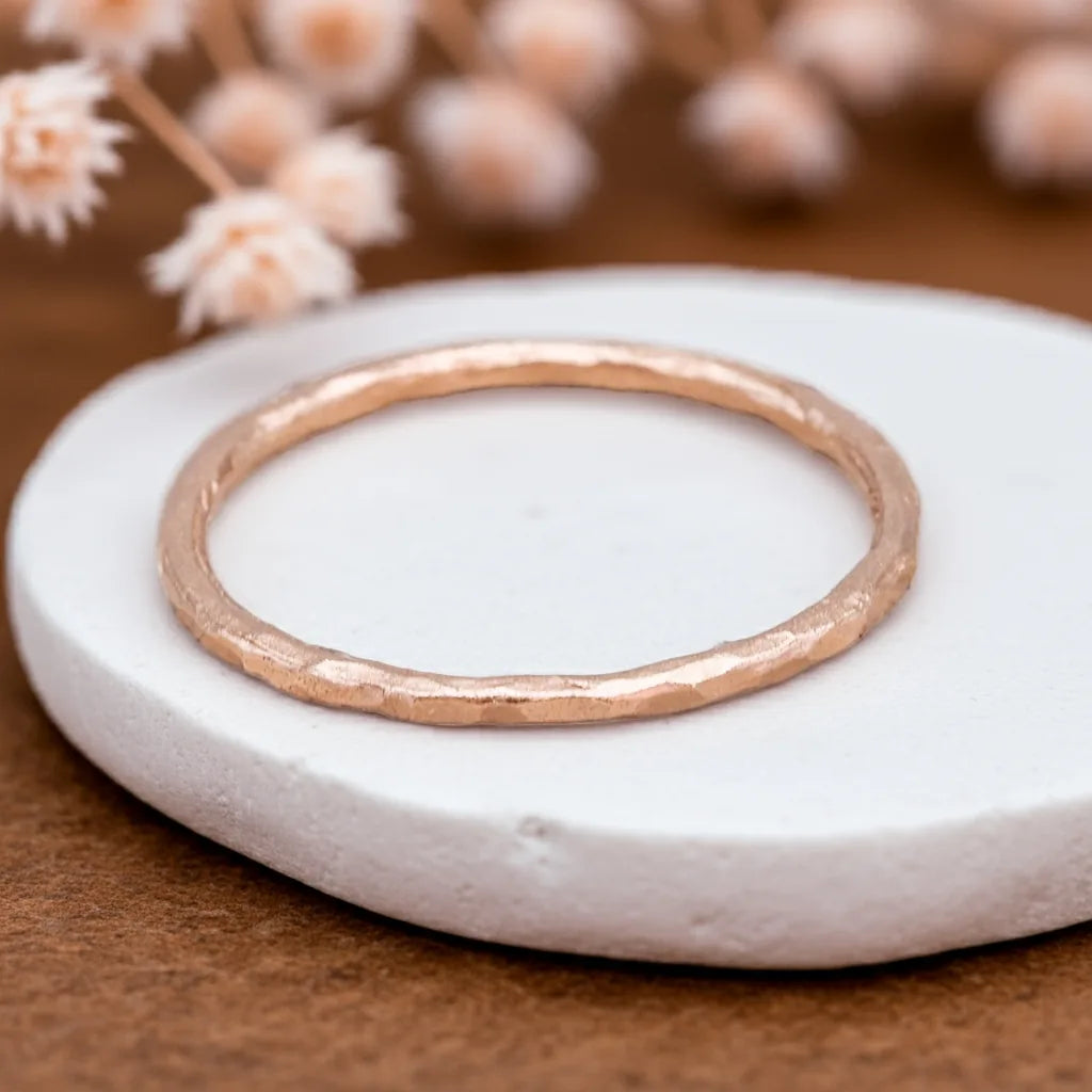 Rose gold ring on a white stone with blurred flowers in the background