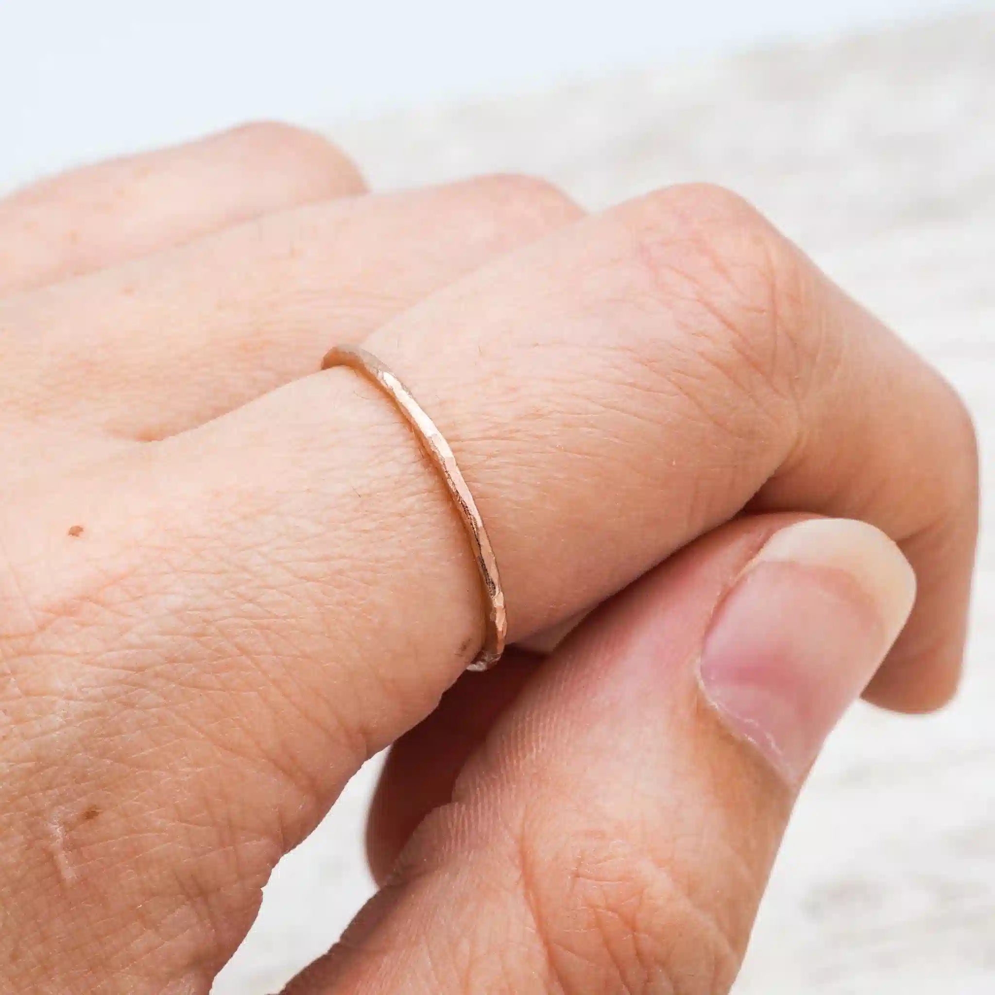 Delicate rose gold hammered stacker ring worn on a hand, showcasing its lightweight design and textured finish.