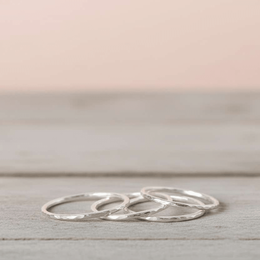 Set of silver rings on a light wooden surface with a soft pink background